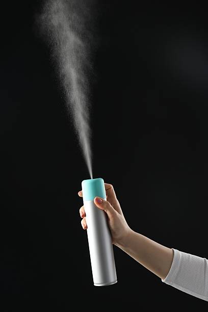 woman spraying air freshener on black background, closeup