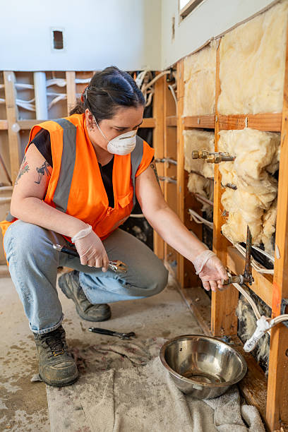 a female plumber kneels down to check the plumbing fittings